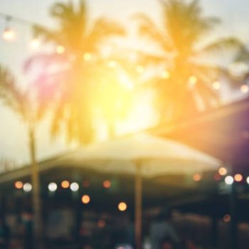 blurred bokeh light on sunset with yellow string lights decor in beach restaurant